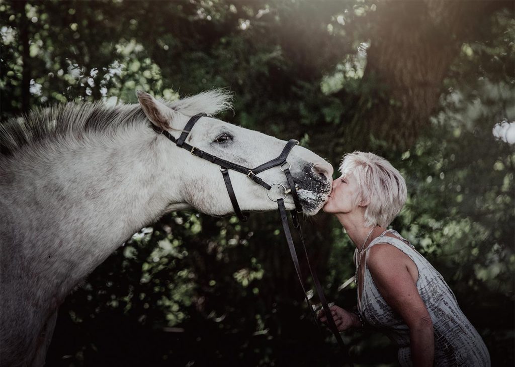 Photo of Salli Deighton kissing her horse in a wooded area.