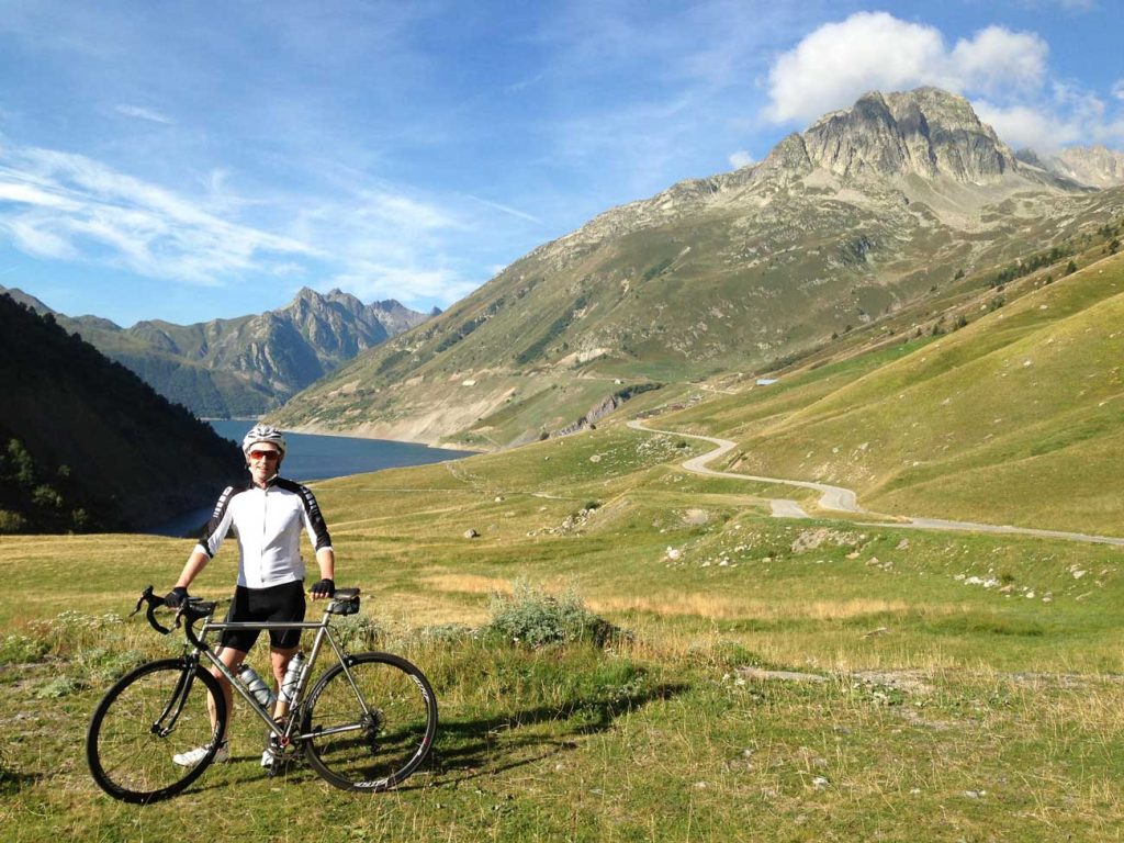 Photo of Simon Gleave with his bike at the end of a trail through a mountain range with a lake at the foot of the mountains.